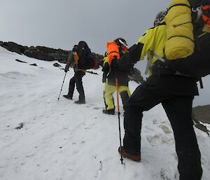 Three expeditoners on a training hike crossing an ice covered rise with a thin coating of snow without spiked chains