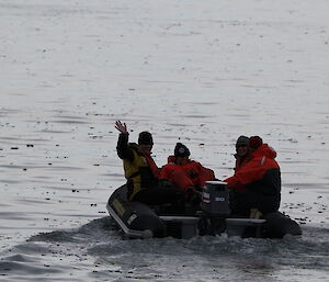 Four expeditioners look back at the camera from a moving inflatable rubber boat