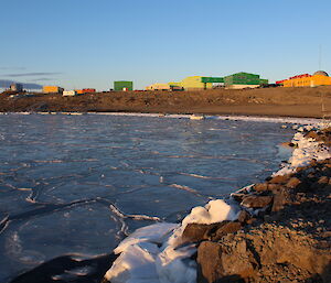 Pancake ice in the foreground with Davis station behind set against a clear blue sky