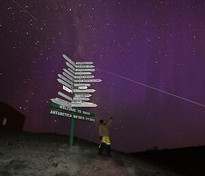 Aaron Stanley pointing to the sky where there is a reddish purple glow of the aurora australis