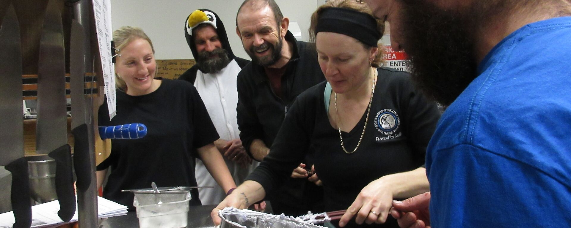 Two female and three male expeditioners making marshmallows in a stainless steel commercial kitchen. One man is dressed as a penguin.