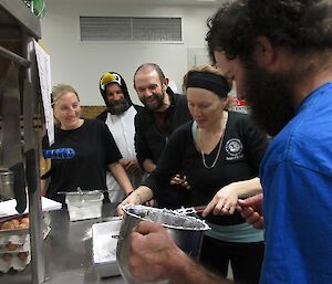 Two female and three male expeditioners making marshmallows in a stainless steel commercial kitchen. One man is dressed as a penguin.