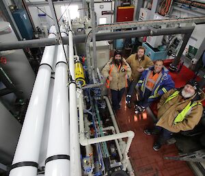 Darren White, Scott Visser, Vas Georgiou and Paul Deverall readying standing in the reverse osmosis plants and looking up to the camera — large pipes at left of frame
