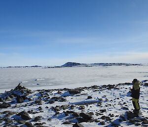 Law cairn looking north across the newly formed sea ice, an expeditioner stands on rocks and snow looking away from camera