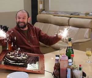 John Parker at Davis station being served his birthday cake along with a lit sparkler in each hand — he is grinning broadly