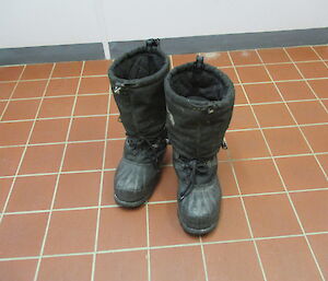 A pair of winter glacier boots sitting on a tiled floor