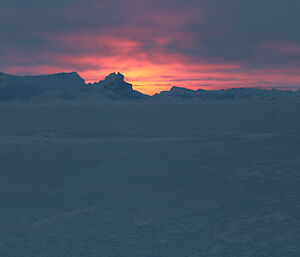 A stunning pink and orange sunset — the only sign of in the sun that day — with icebergs in the foreground — a view on the sea ice on the way back to Davis