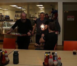 Darren White and Vas Georgiou deliver a cake and sparklers to Brett Sambrooks on the occasion of his birthday