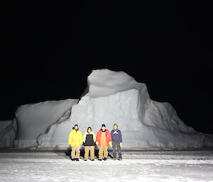 Chris Burns, Jen Proudfoot, Vas Georgiou and Scott Visser in front of an iceberg while standing on the sea ice — in the dark