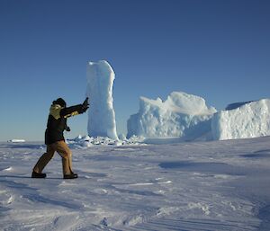An optical illusion with an expeditioner appearing to push a tall iceberg over