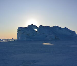 The sun shining through a hole in a large iceberg