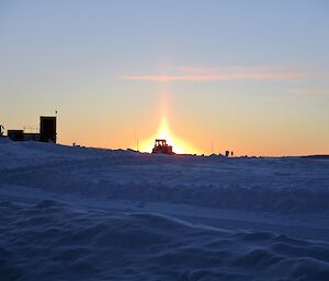 A picture of the Davis dozer on the snow with the morning sun behind it