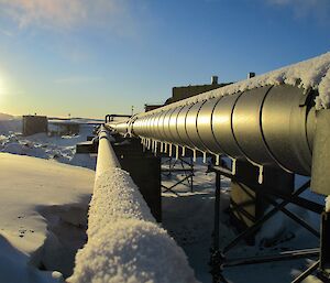 A large pipe which is part of the station site services, with ice and snow defrosting in the sun at Davis