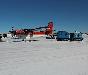 People gathered around plane to unload and tie it down. Blue Hägglunds at rear.