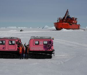 Ali and Kirsten wave to us standing in front of the pink Hagg, Opal, which is parked on the sea-ice having been taken off the main sea-ice road and onto the ungroomed sea-ice to see how she handles. In the background is the Aurora Australis parked in the sea-ice surrounded by utes, trucks and other Haggs loading up with supplies being unloaded from the ship during re-supply.