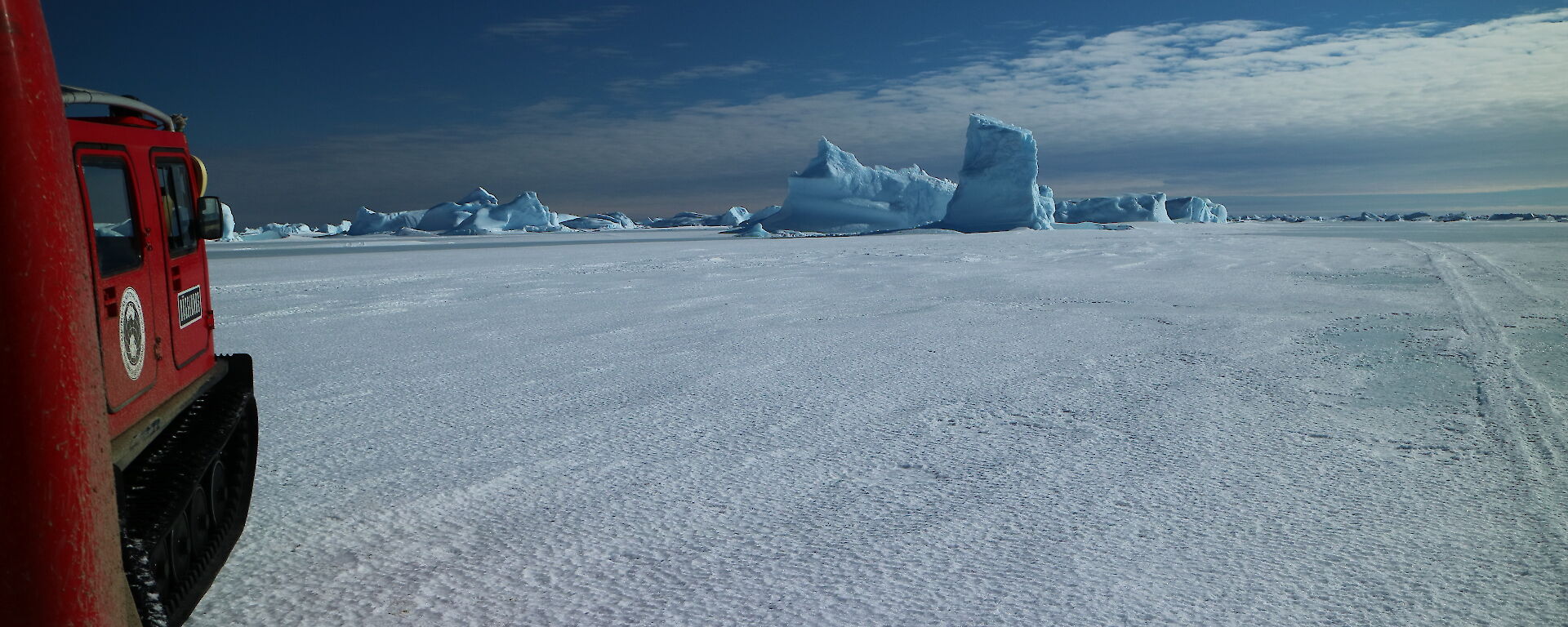 Hägglunds about to drive past a blue iceberg stuck in the sea ice.