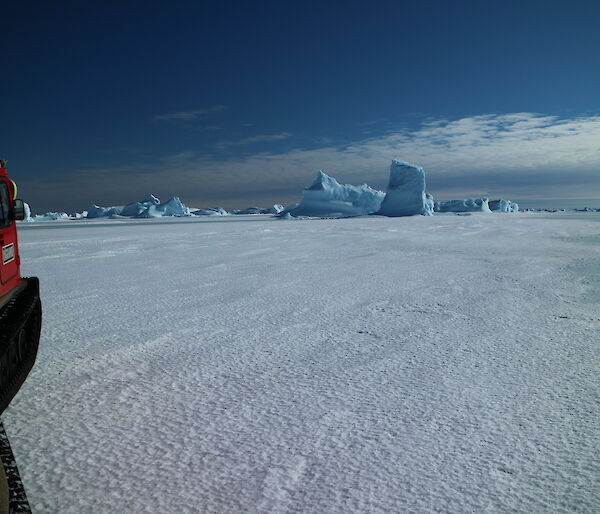 Hägglunds about to drive past a blue iceberg stuck in the sea ice.