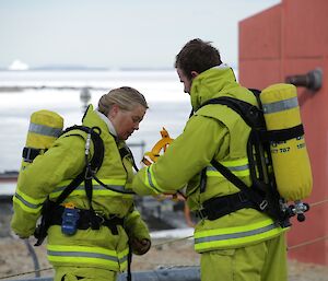 Kerryn (chef) and Jock (Mechanic) are in yellow fire fighting gear, preparing their breathing apparatus — tank on their back and a full face mask — before they enter the smokey Emergency Power House building. They will go into fight the fake fire and look for the missing person as part of the drill.