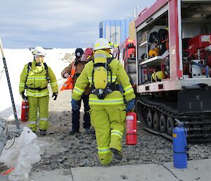 Kerryn and Jock are in full fire fighting gear, with their breathing apparatus gear on, standing beside the Fire Truck Hagglund, carrying hand-held extinguishers in preparation for entering the building with the “fire”.