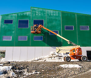 Two tradies are on the elevated work platform, wearing safety gear, cleaning windows on the second storey of the Living Quarters building.