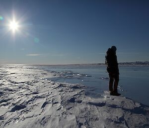 Nick stands next to a frozen lake on the top of the glacier. The lake ice is smooth whereas the glacier ice is highly textured from the wind.