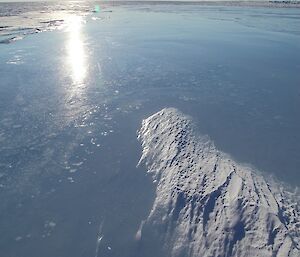 There is a texture pattern of snow on the smooth blue smooth surface of the frozen glacier lake