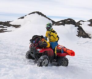 Rhys is driving a quad bike through soft snow up a slope.