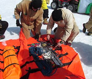 A tarpaulin is laid out on the sea-ice. In it you can see a number of tools to use if there is a problem with the bike or you need shelter.