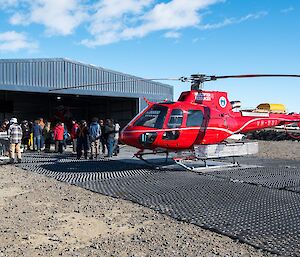 A Bell helicopter is on the helipad. Behind the helicopter are people standing around socialising before the BBQ starts.