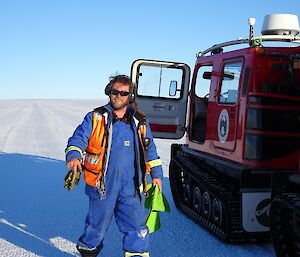 Trevor is carrying markers to put out on the ice runway. He is standing next to a Hägglunds.