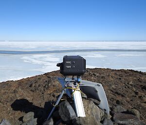 A camera is on a tripod, located on an Antarctic island, aimed towards penguins which are out of view of the photo.