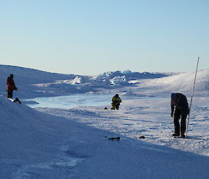 Three team members can be seen working in a depressed are near the melt pond on the glacier.