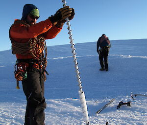 An expeditioner is holding a 2m length of drill bit, used to make holes in the ice for deploying equipment into the frozen lake.