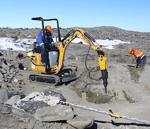 Danny is in a small digger, digging a hole for the Infrasound building footings. Large boulders surround the machine.
