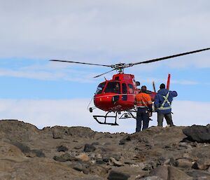 David and Adon are watching the helicopter leave the fieldsite. The helicopter is still hovering close to the ground at the start of its takeoff.