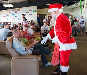 Everyone is sitting in the Living Quarters building, lounging on couches, looking relaxed. Father Christmas is handing Al his present.