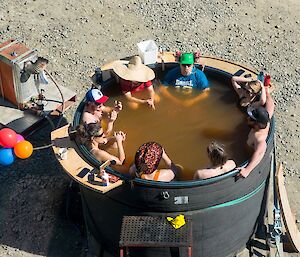 Nine people are sitting in a home made hot tub, looking very relaxed.