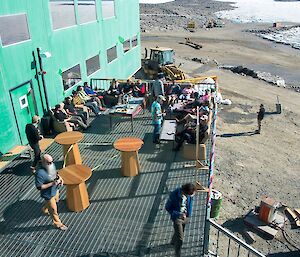 Expeditioners are sitting in couches, outside on the deck of the Living Quarters. Everyone is looking very relaxed.