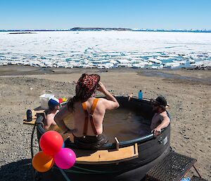 Three people are in the hot tub. In the background you can see sea-ice in the bay.