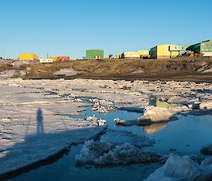 The foreground is a bay covered in sea ice. On the hills behind sit the colourful buildings of Davis station.