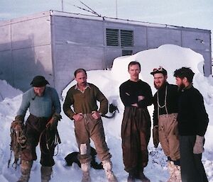 Five men stand in front of the old powerhouse. These are the winterers from 1957: Nils Lied, Bruce Stinear, Bob Dingle, Alan Hawker and Bill Lucas.