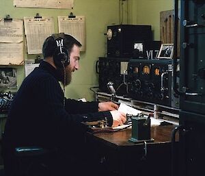 Alan Hawker is sitting at the comms desk, with headphones on, operating the radio.