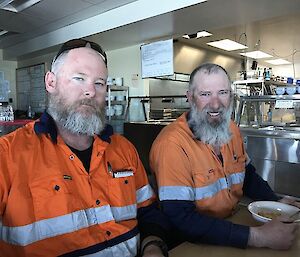 Two men sitting in the kitchen relaxing after working outside.