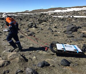 A man pulling a ground penetrating radar over the rocks.