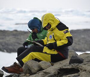 Nick and Marcello are sitting on the ground, studying rocks.