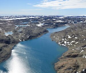 An aerial view of several lakes within the Vestfold Hills. The land is brown and rocky while the lakes are a beautiful blue. The sun is also shining.