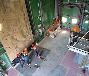 An aerial view of the climbing wall inside the Greenstore. One person is roping up, preparing to climb, while three others help.