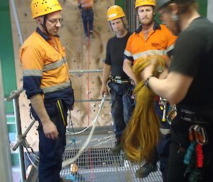 Fitzy, Rhys and Bryce are watching Chris show them how to tie rope for abseiling.