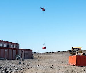 The helicopter is slinging the Trajer melon back into station. It is flying low, approaching the helipad. The workshop is seen in the foreground.