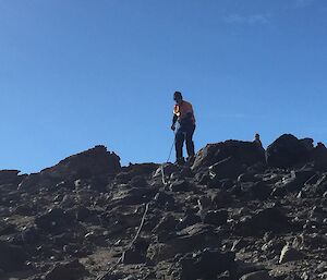 A person is seen on a high point, pulling a long cable towards them. The ground is very rocky.